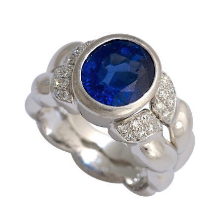 19376 Double Flowing Lines Blue Sapphire Ring Designed & Handmade by Kaufmann de Suisse in 18kt White Gold featuring one Bezel Set Oval 4.83cts Blue Sapphire mounted with 32 Round Brilliant Cut FV